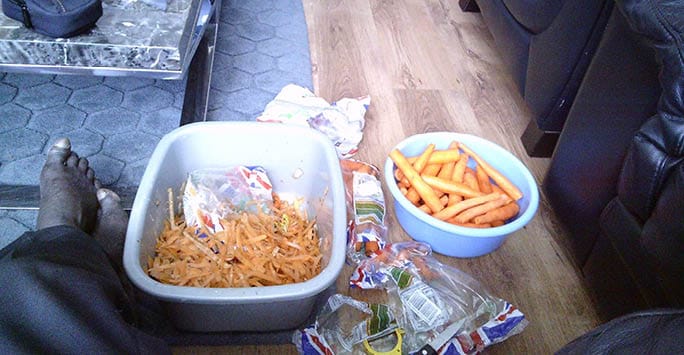 Unhealthy snack food on the floor including a half-eaten burger and copious amount of chips, with a person's feet visible at the bottom; casual environment highlighting nutritional challenges.