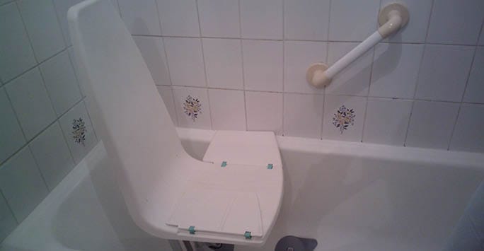 A raised toilet seat installed in a bathroom with tiled walls, designed to aid individuals with mobility issues or frailty, accommodating ergonomic needs for diverse ethnic backgrounds.