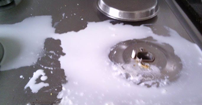 Spilled milk or liquid on a metal surface, possibly a kitchen or work surface, with some utensil or machine part nearby.