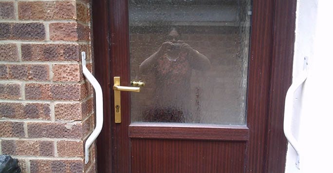 Community entrance door with a glass panel and a person taking a photo reflected in the glass, highlighting access and building security.