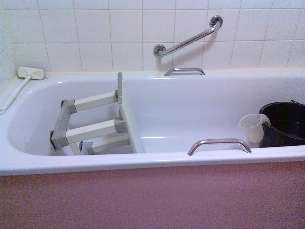Lifting aid in a hospital bath tub, with a bucket and grab rails, designed for patient safety and assistance with bathing for elderly or disabled individuals.