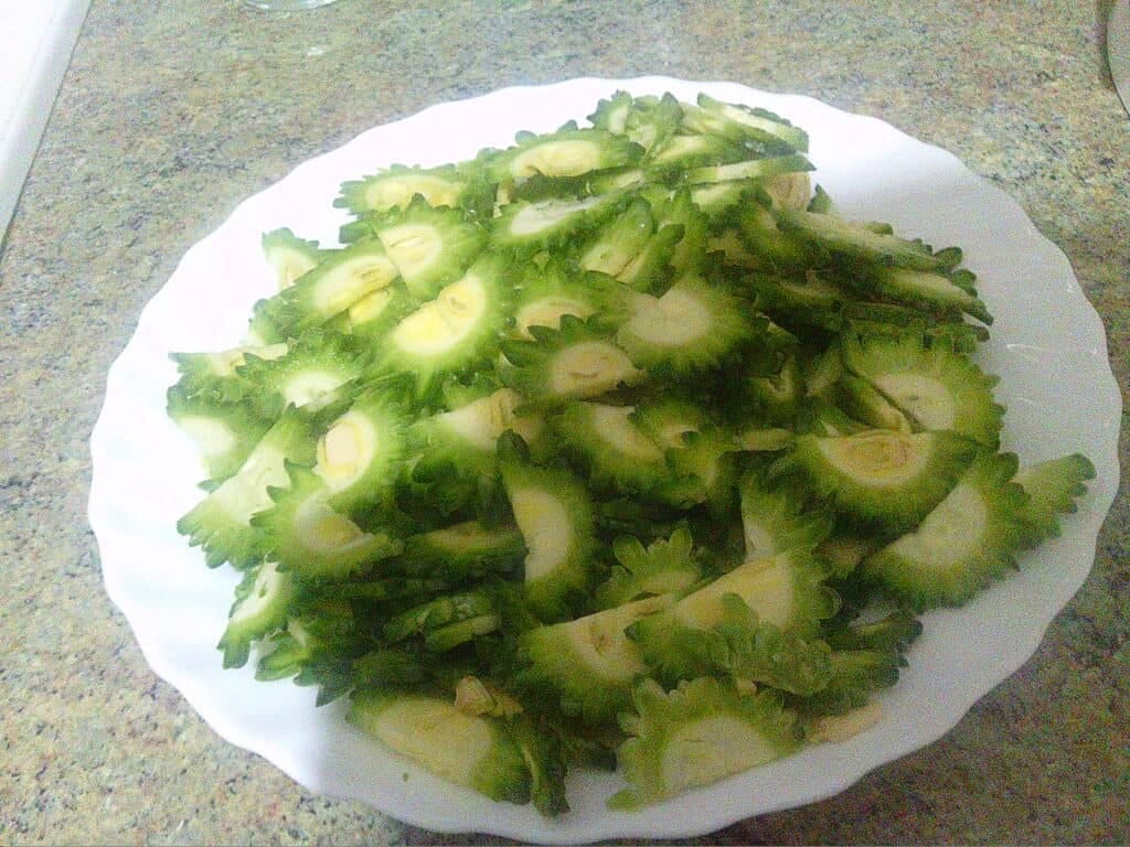 Fresh sliced bitter melon on a white plate, highlighting its green colour and distinctive warty texture, suitable for a healthy diet and nutritional research on frailty and ethnicity.