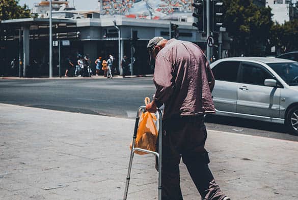 Elderly person using a walking aid on a city street, highlighting issues of frailty and ageing.